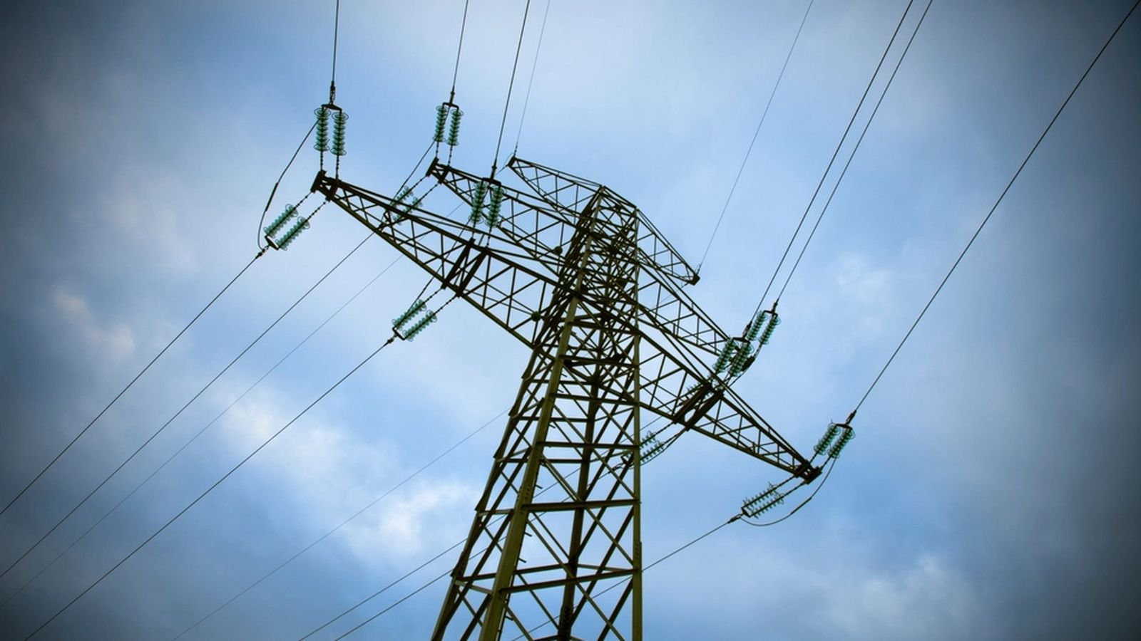 Pylône de ligne électrique haute tension vu en contre-plongée sous un ciel nuageux