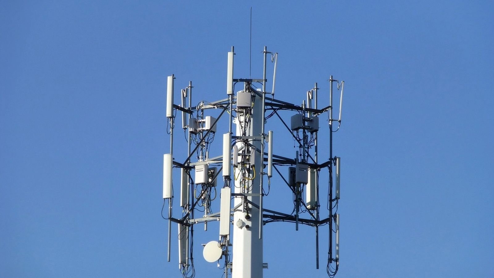 Sommet d’un pylône de télécommunications équipé d’antennes de téléphonie mobile sur fond de ciel bleu
